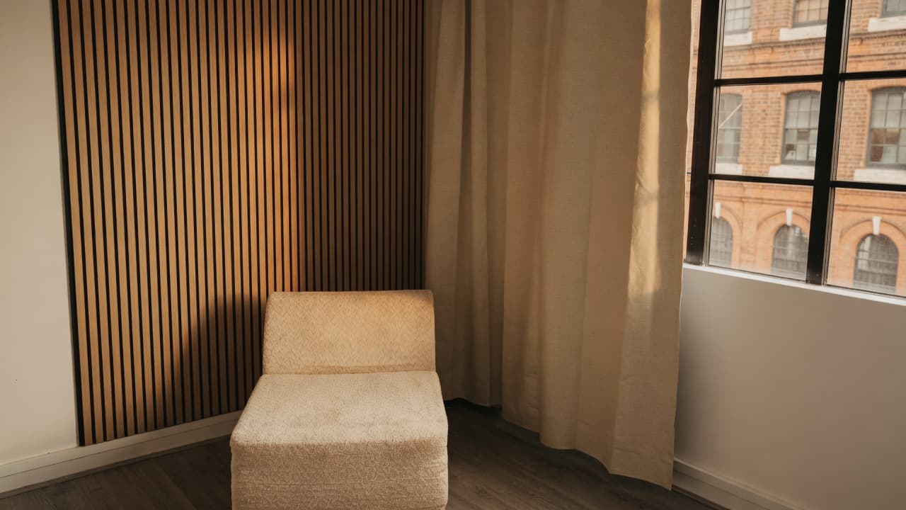 The Content Suite interview nook — oak slat wall, cream chair, linen curtain and warehouse windows