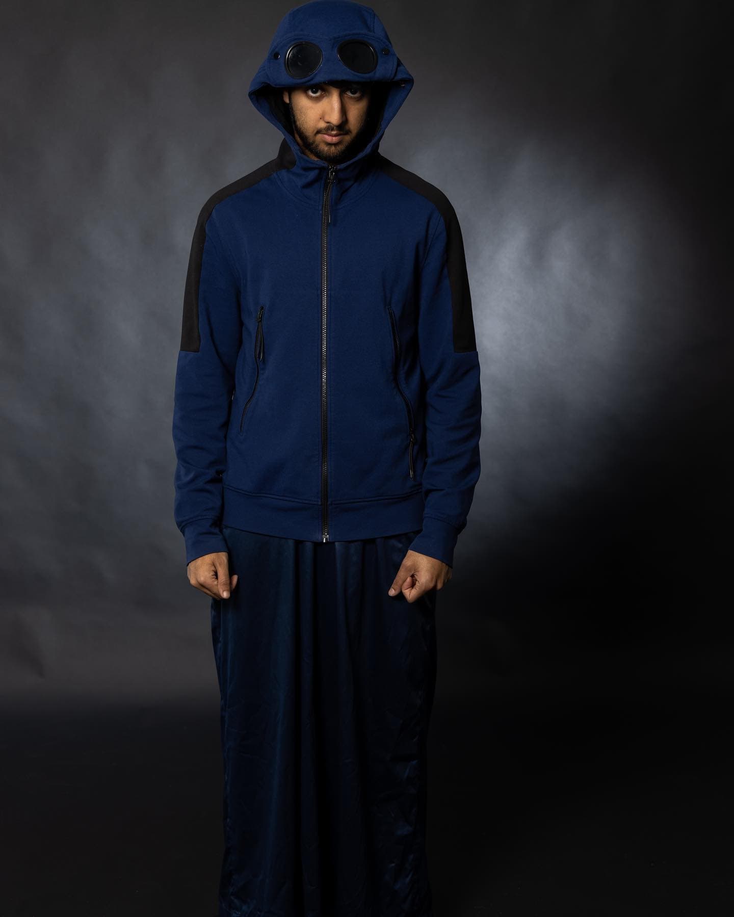 Studio portrait — model in a navy goggle-hood jacket against a lit grey backdrop