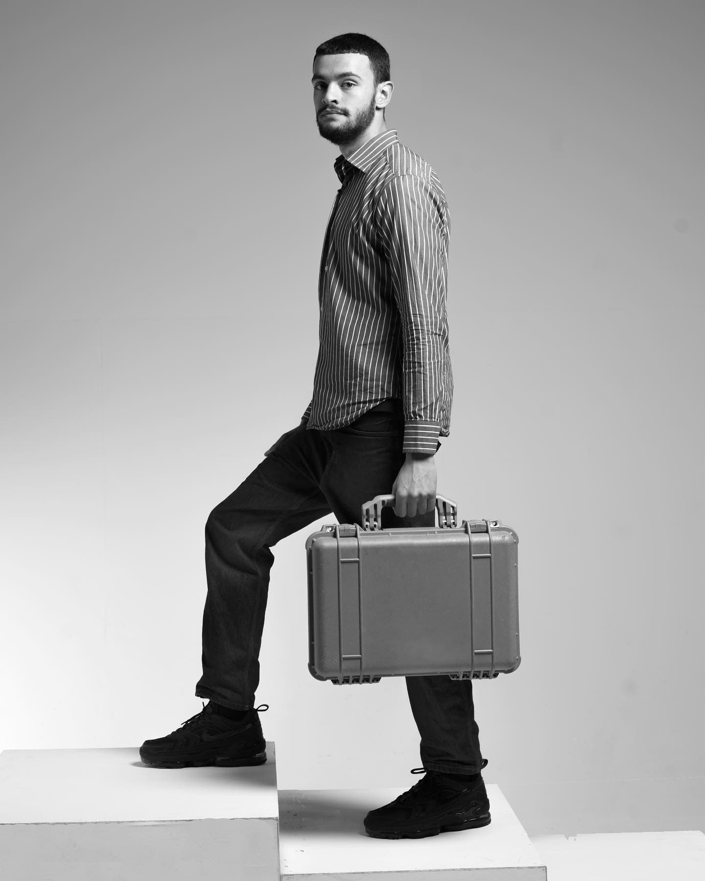 Black-and-white studio portrait — man stepping up holding a hard equipment case